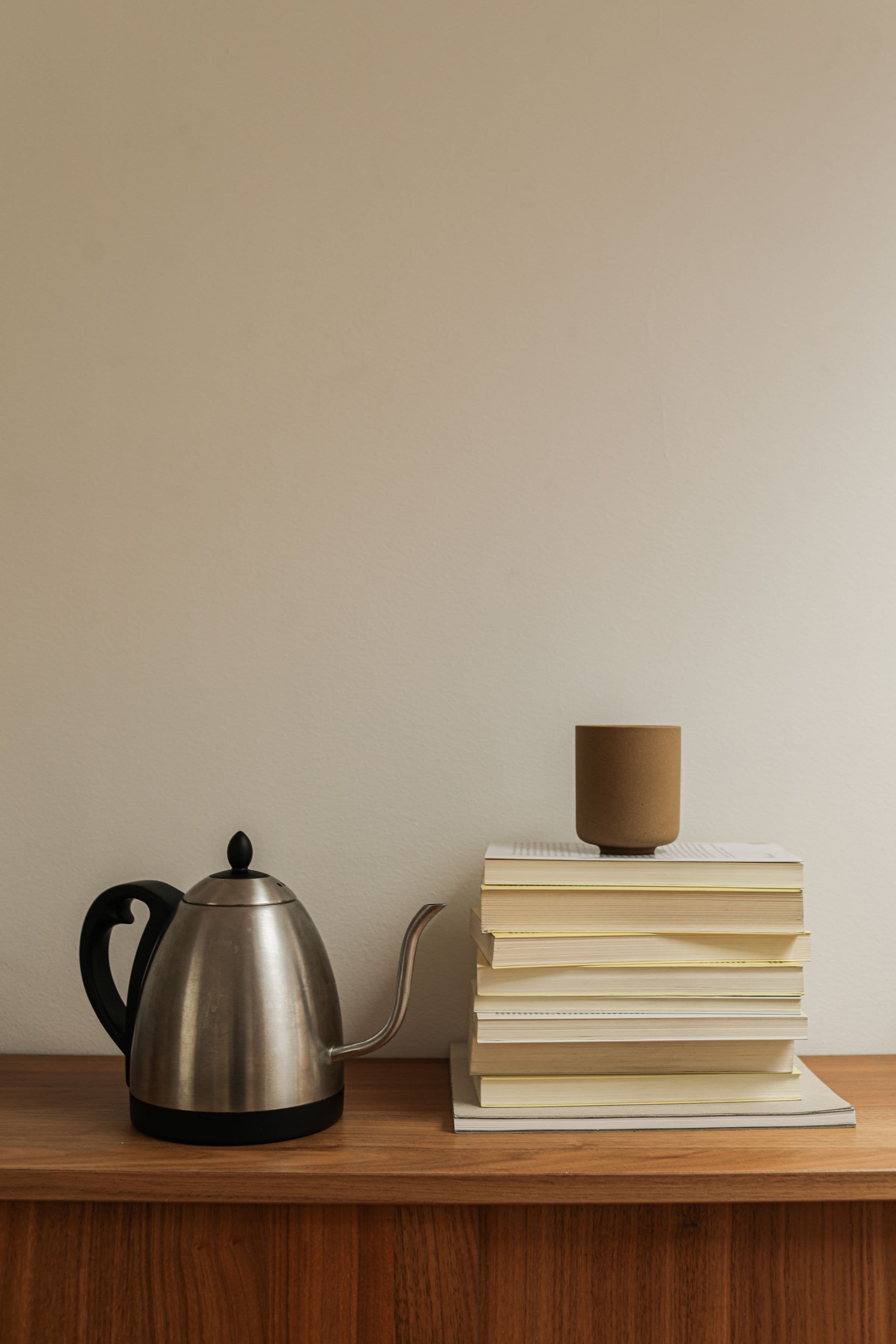 A ceramic cup, books, and kettle arranged on a wooden surface